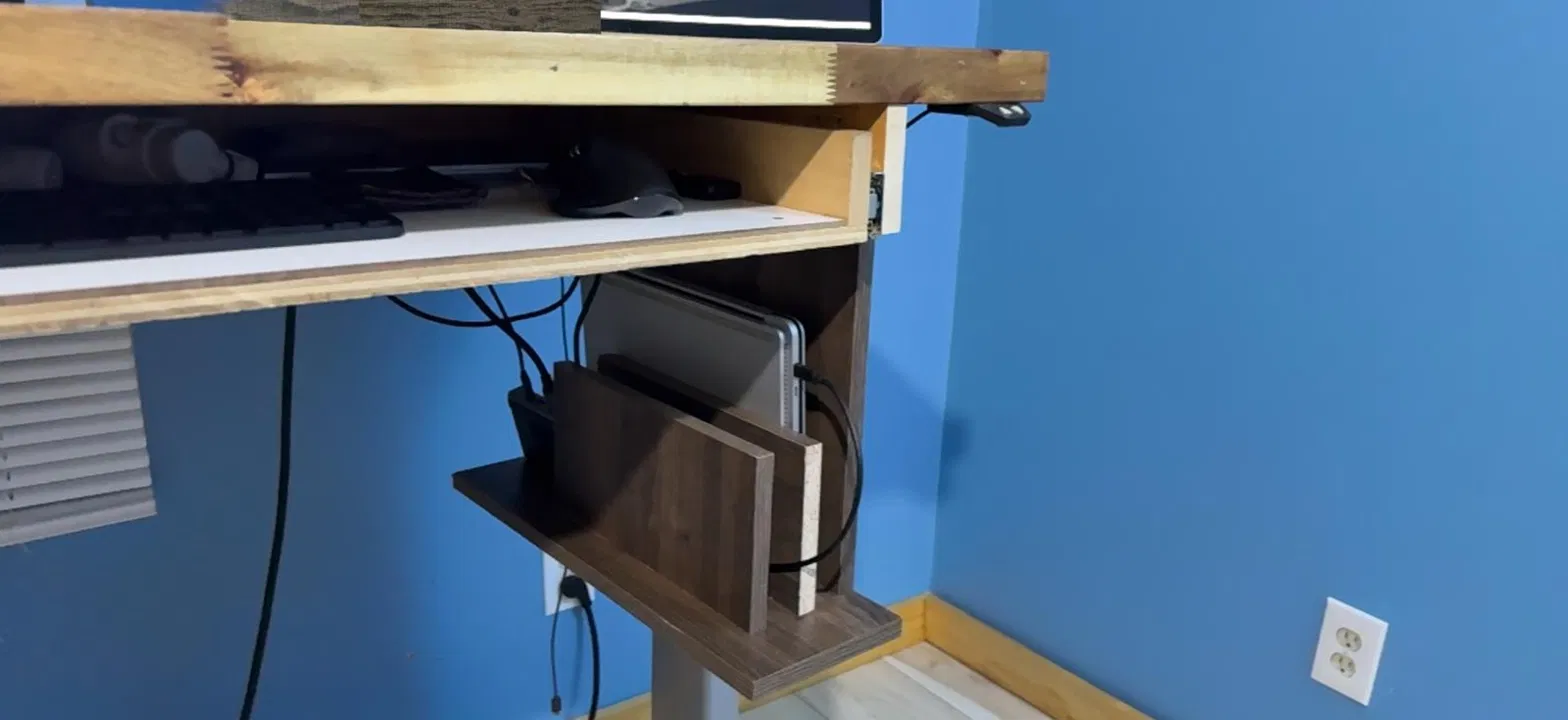 The finished mockup attached to the side of the drawer box under the butcher block desktop, holding the closed laptop upright with the docking station beside it